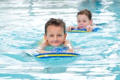Zwei Kinder im Wasser, die ein Schwimmbrett benutzen