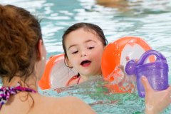 Ein junges Kind mit Schwimmflügeln und eine Person mit Gießkanne